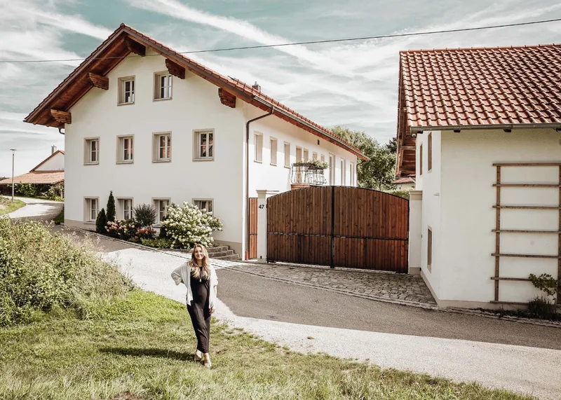 Das Haus von der Straße: weiße Fassade, Hortensien, das Holztor und Sabrina davor auf der Wiese.