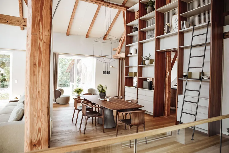 Der Essplatz im Wohnzimmer-Loft: Nussbaumtisch mit Stühlen vor der raumhohen Regalwand mit Leiter.