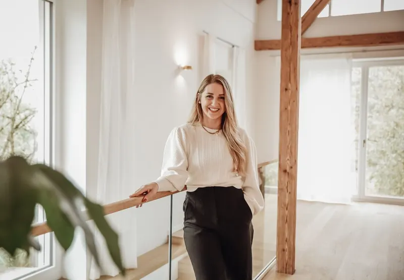 Sabrina lehnt am Geländer im Wohnzimmer-Loft, hinter ihr die alten Balken.