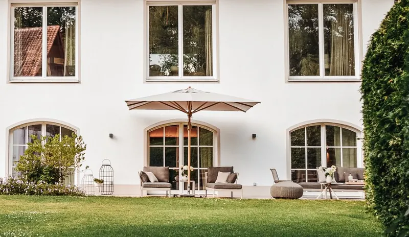 Die Terrasse vor den Bogenfenstern mit Loungemöbeln und Sonnenschirm.